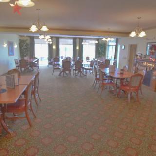 A spacious dining area with multiple tables and chairs, illuminated by chandeliers.