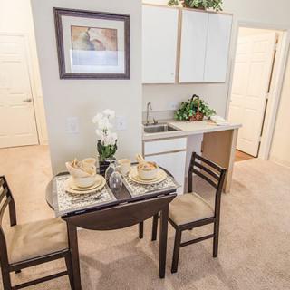 A cozy dining area with a small table and kitchenette setup, featuring simple decor and elegant tableware.