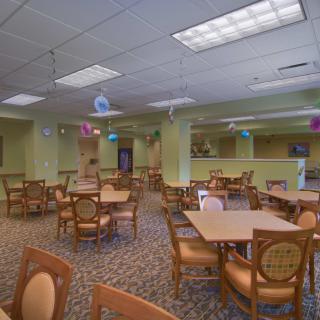 An empty dining area with neatly arranged tables and chairs, featuring a carpeted floor and ceiling lights.