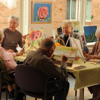 A group of seniors engaged in a painting class, working on their individual art pieces.