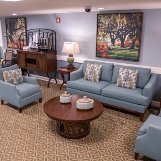 A cozy living room featuring blue sofas and armchairs, a wooden coffee table, and decorative artwork on the walls.