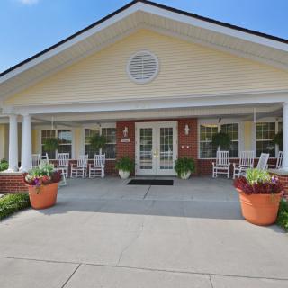 The front entrance of a building with a porch, columns, and potted plants.