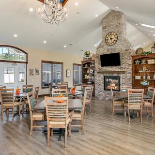 A spacious dining area featuring a fireplace, wooden tables and chairs, a chandelier, and a vaulted ceiling.