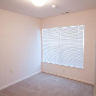An empty room with carpeted flooring and a large window covered with blinds.