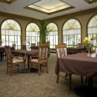 A cozy dining area with tables and chairs, featuring large arched windows.