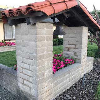 A charming stone structure with a tiled roof, featuring vibrant pink flowers in a garden setting.
