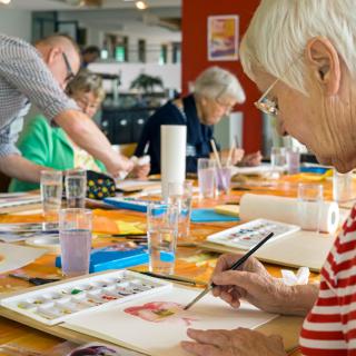 A group of seniors engaged in a painting class, using watercolors to create their artwork.