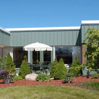 A modern building with a landscaped garden and patio area featuring a white umbrella.