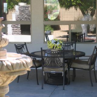 A serene outdoor patio setting with a fountain, table, and chairs surrounded by lush greenery.