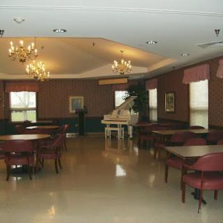 A spacious dining room featuring round tables, elegant chandeliers, and a grand piano.