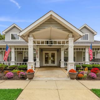 A welcoming entrance of a house with a front porch, decorated with flags and surrounded by landscaped gardens.