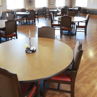An empty dining area with round tables and chairs on a wooden floor.