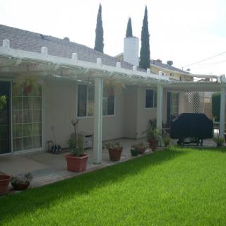 A backyard view with a patio area, lush green grass, and potted plants.
