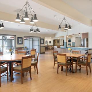 A spacious dining area with modern design elements, featuring multiple tables and chairs under stylish lighting fixtures.