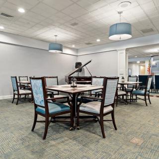 A dining area featuring neatly arranged tables and chairs, with a grand piano in the background.