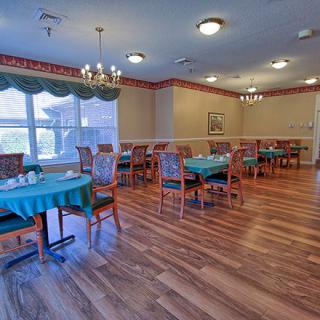 An elegant dining area with wooden flooring, set with tables and chairs, enhanced by natural light from large windows.