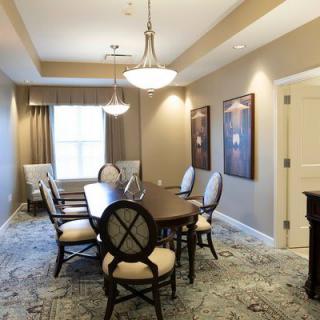 A well-furnished dining room with a central table surrounded by chairs, elegant lighting fixtures, and decorative artwork on the walls.