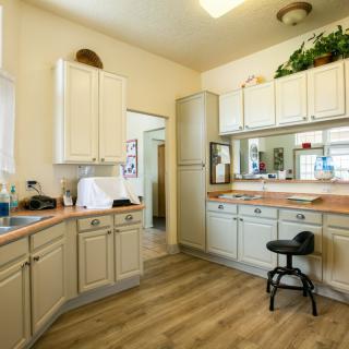 A bright kitchen interior with cream-colored cabinets, wooden flooring, and a workstation stool.