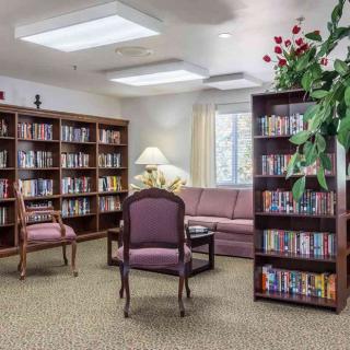 A cozy library reading area with bookshelves, a sofa, chairs, and a lamp.