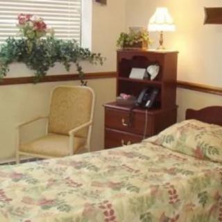 A cozy bedroom with a single bed, a bedside lamp, a chair, and shelves.