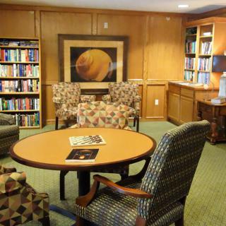 A cozy library reading area with shelves filled with books, a round table, and comfortable chairs.