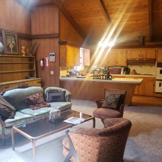 A cozy living room with vintage decor and wood paneling, featuring a comfortable seating area and adjacent kitchen.