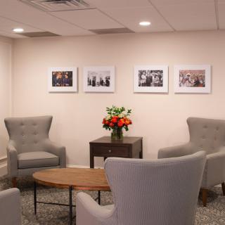 A cozy waiting room with comfortable chairs, a wooden table, and framed pictures on the wall.