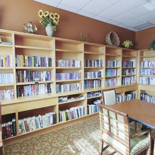 A cozy library reading room with wooden bookshelves filled with books, a table, and chairs.