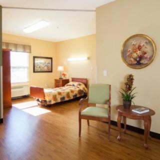 A cozy bedroom featuring a bed, side table with a lamp, chair, and decorative elements on the wall.