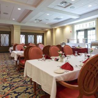 An elegant dining room setup with tables and chairs neatly arranged, adorned with red napkins and place settings.
