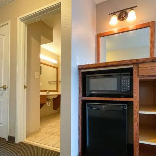A hotel room with a view of the bathroom entrance, featuring a small kitchenette area with a microwave and refrigerator.
