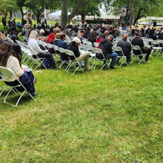 A gathering of people seated on chairs in an outdoor setting.
