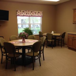 A cozy dining room with multiple tables and chairs, a television on the wall, and a window providing natural light.