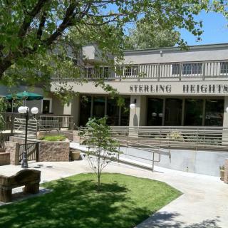 Sterling Heights building surrounded by trees and greenery with benches in the foreground.
