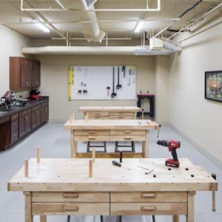A spacious woodworking workshop featuring multiple workbenches, a drill, and storage cabinets.