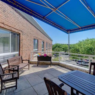 A serene outdoor patio space featuring a blue canopy, wooden furniture, and a view of lush greenery.