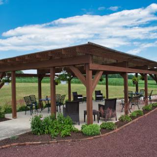 A cozy outdoor pavilion with seating, surrounded by a lush landscape under a clear blue sky.
