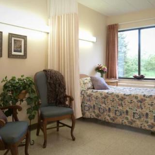 A cozy bedroom with classic decor, featuring a bed, chairs, and a large window.