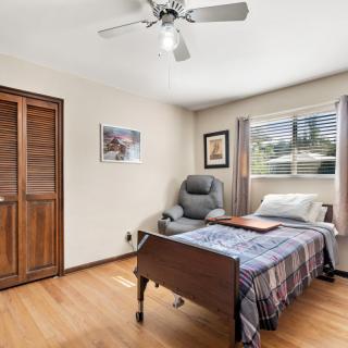 A cozy bedroom with a hospital bed, armchair, and window allowing natural light.