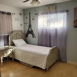 A cozy bedroom with a single bed and Eiffel Tower wall decor, featuring pastel curtains.
