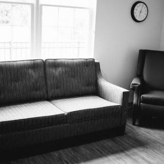A minimalist living room setup featuring a couch, a chair, and a wall clock.