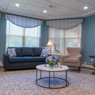 A cozy living room with a sofa, armchair, and coffee table set against large windows with elegant curtains.
