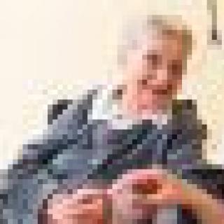 An elderly person smiling while sitting indoors.