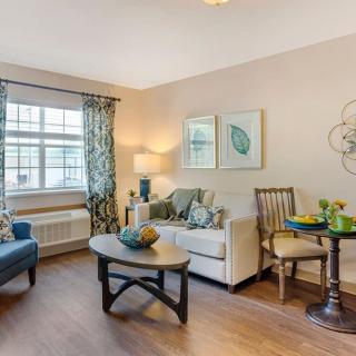 A cozy living room with modern decor, featuring a sofa, coffee table, and natural light from a large window with curtains.