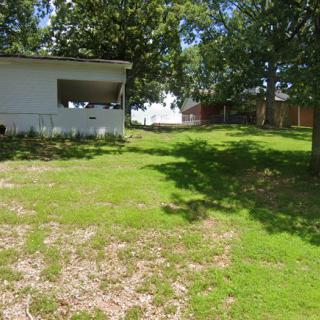 A house with a grassy yard and surrounding trees on a sunny day.