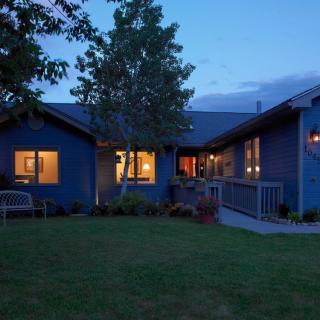 A cozy house with illuminated windows at dusk, surrounded by a grassy yard and trees.