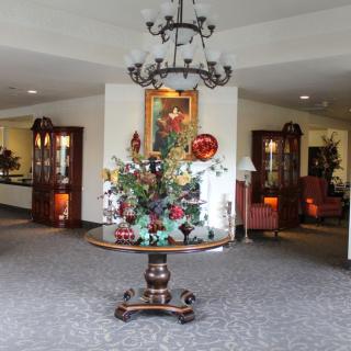 A beautifully decorated lobby featuring a central table with a flower arrangement under an ornate chandelier.