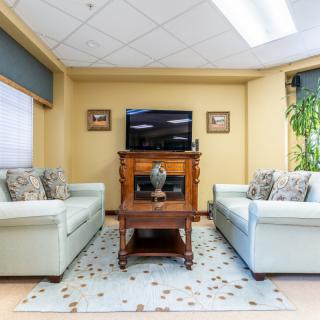 A cozy living room with two sofas and a central wooden coffee table, featuring a TV mounted on the wall.