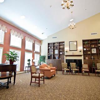 A spacious living room with a library and seating area, featuring large windows, bookshelves, a chandelier, and carpeted flooring.