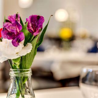 A small vase with vibrant flowers serves as a table centerpiece in an elegantly set dining area.